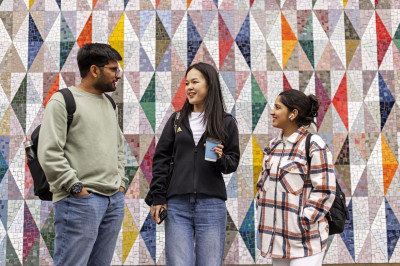 Three students talking in front of a patterned wall