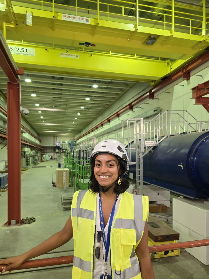 Anika in a highvis jacket and hard hat, at her workplace of CERN