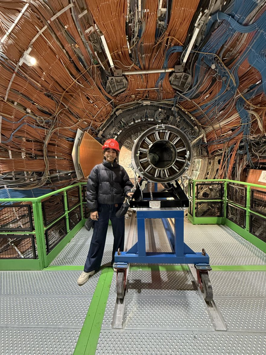 Krishni smiling in a hard hat, standing next to the hadron collider 