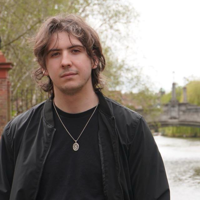 Lyrkan standing in a park in front of trees and a river