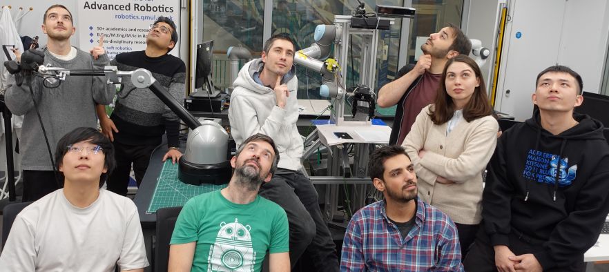 Dr Lorenzo Jamone and a selection of Robotics students, looking upwards as they pose in the lab