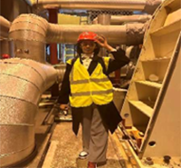 A student in a high vis vest and a hard hat poses on an industrial site visit