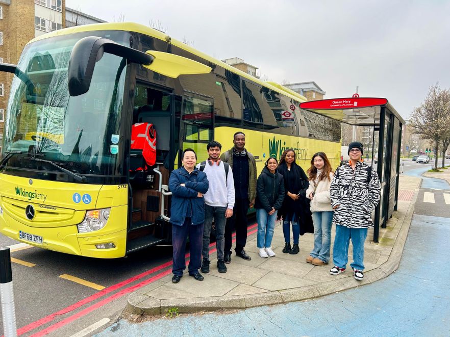 A group of students in front of a yellow tour bus 